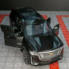 A black 1:32 diecast Cadillac Escalade pull-back model car displayed on a gray surface.