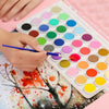 A hand is using a brush to apply watercolor paint colors onto paper in a portable set.