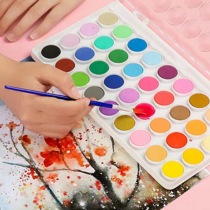 A hand is using a brush to apply watercolor paint colors onto paper in a portable set.
