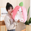A young woman holds a pink fruit bunny plush toy with green leaves in a soft light.
