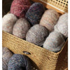 A collection of multicolored soft alpaca blend yarn skeins in various shades and textures stored in a woven basket.