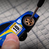 A close-up of a blue RC drift car model with gold wheels and a finger holding the throttle mechanism.