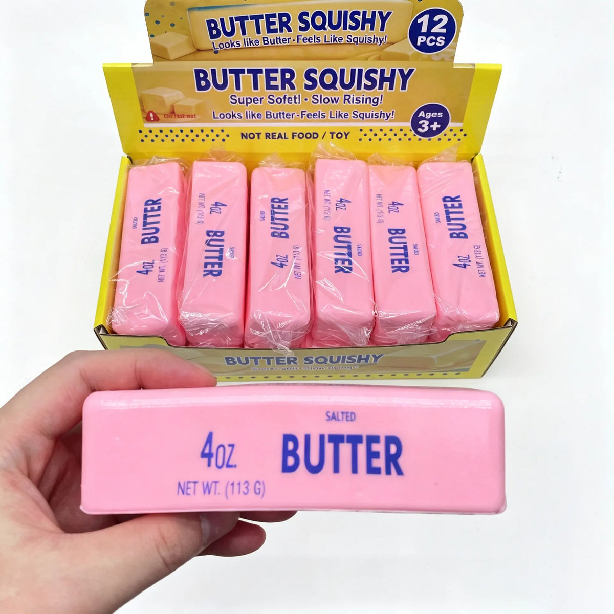 A hand holds a pink butter squishy toy next to its packaging box.