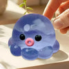 A translucent blue octopus squishy stress ball is held by a hand on a white surface.