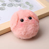 A pink fluffy plush pig keychain with black eyes and a pink tag, resting on a light wooden frame.