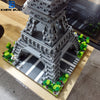 A detailed miniature model of the Eiffel Tower built from gray LEGO-style blocks, set on a green landscape.