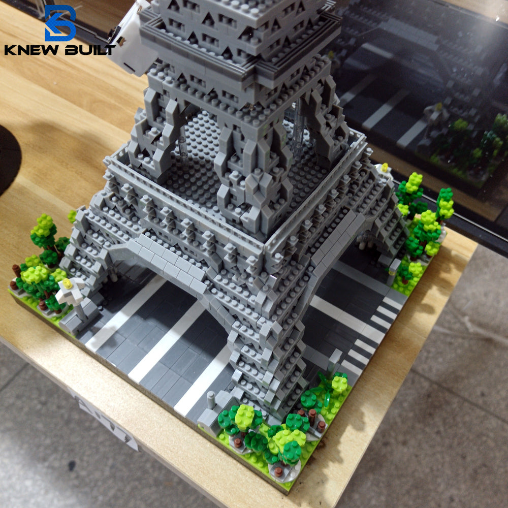 A detailed miniature model of the Eiffel Tower built from gray LEGO-style blocks, set on a green landscape.