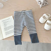 A pair of navy and white striped baby leggings lying on a wooden surface next to a book and white shoes.
