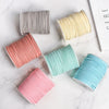 A collection of rolled braided ribbon in various shades of pink, yellow, and blue on a white marble surface.