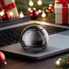 A silver metal fidget spinner resting on a laptop keyboard with festive holiday lights in the background.