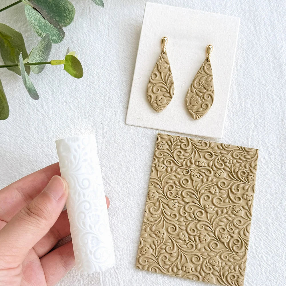Two gold-toned floral texture rollers for polymer clay and crafting displayed on a white surface.