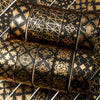 A set of twenty rolls of black and gold foil washi tape stacked horizontally on a patterned surface.