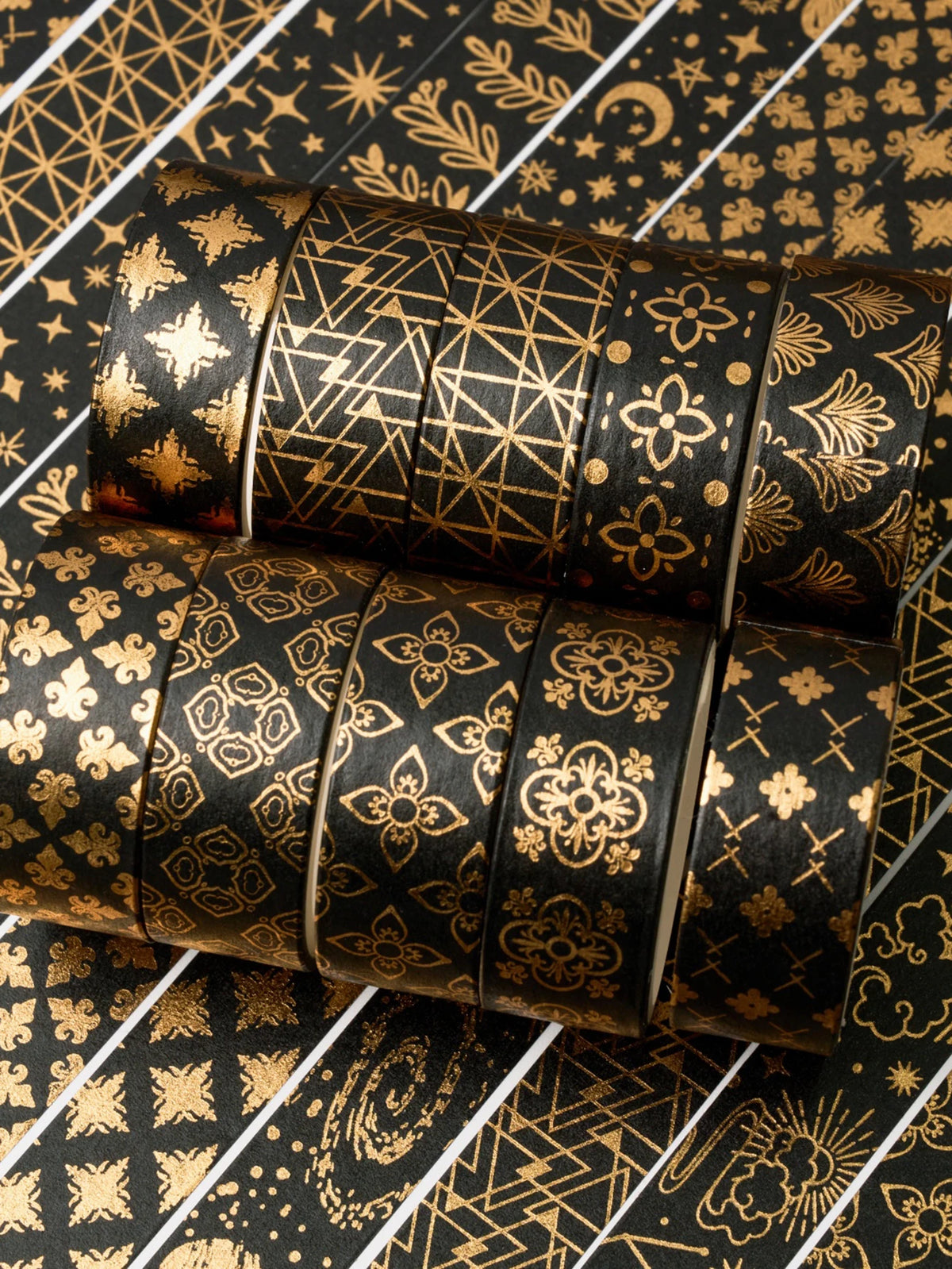 A set of twenty rolls of black and gold foil washi tape stacked horizontally on a patterned surface.