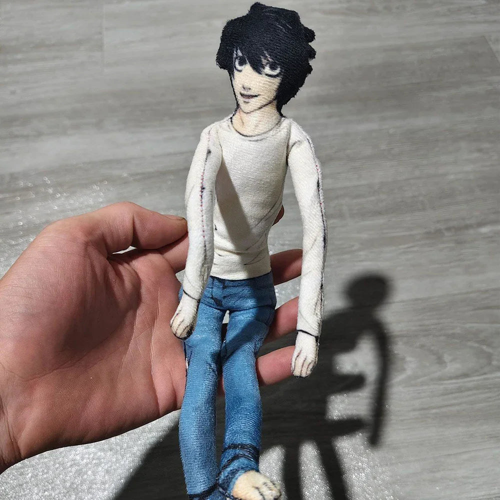 A hand holds a poseable L Lawliet plush doll from Death Note, featuring dark hair and blue clothing.