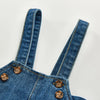 A close-up of a denim romper featuring vertical stitching and brass buttons.