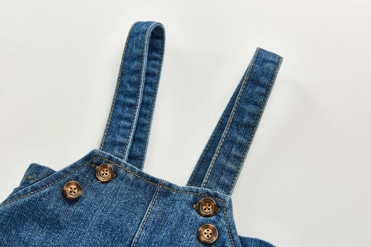 A close-up of a denim romper featuring vertical stitching and brass buttons.