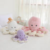 A collection of soft plush octopus toys in pink, purple, and cream colors resting on a white surface.