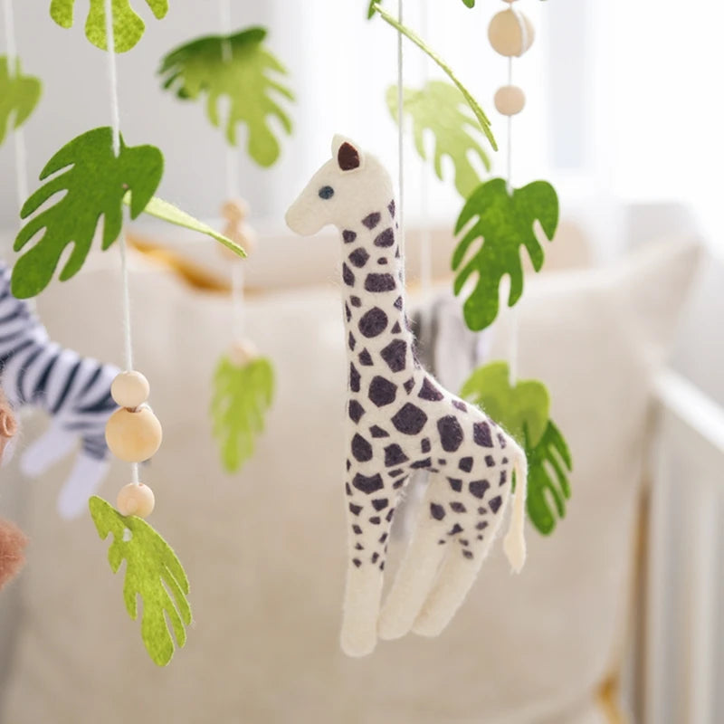 A wooden felt giraffe mobile with green leaves and natural wood beads hanging in a nursery setting.