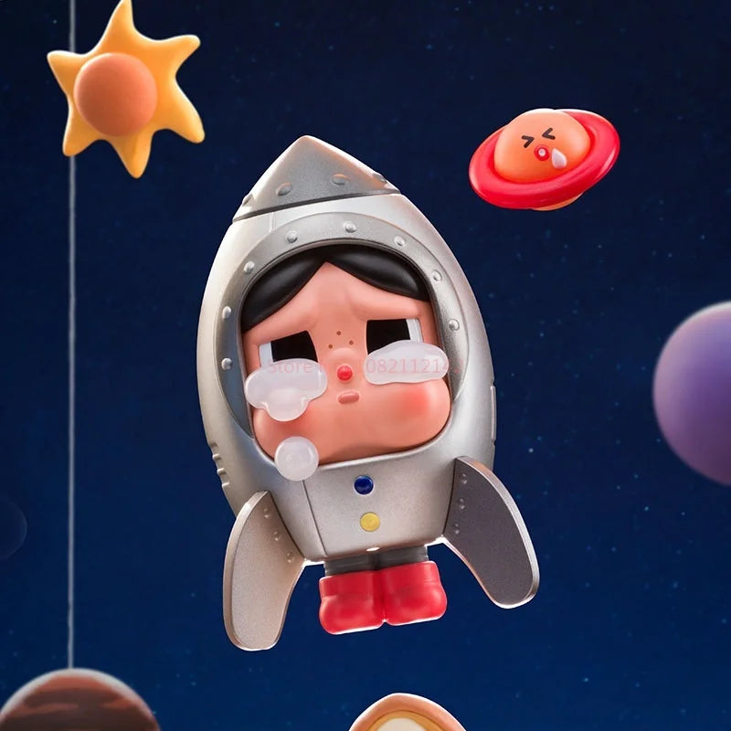 A collectible figurine of a crying baby in a silver rocket suit floating in space with celestial objects nearby.