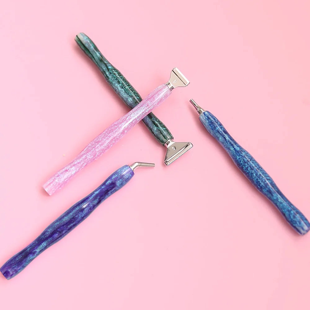A set of five resin diamond painting pens with interchangeable metal tips and multi-placers displayed on a pink background.