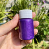 A hand holds a small purple bottle of metallic gold acrylic paint for crafts.