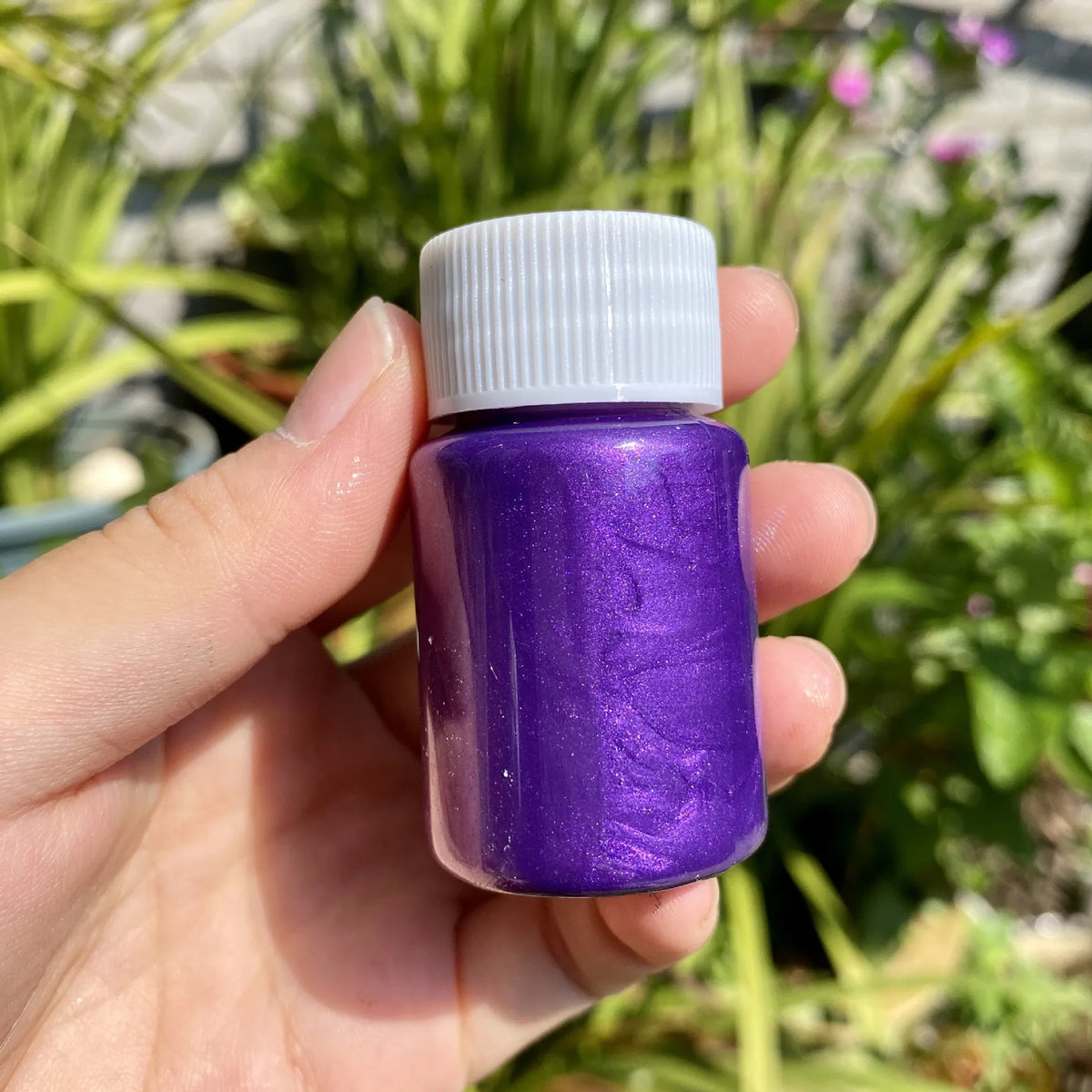 A hand holds a small purple bottle of metallic gold acrylic paint for crafts.
