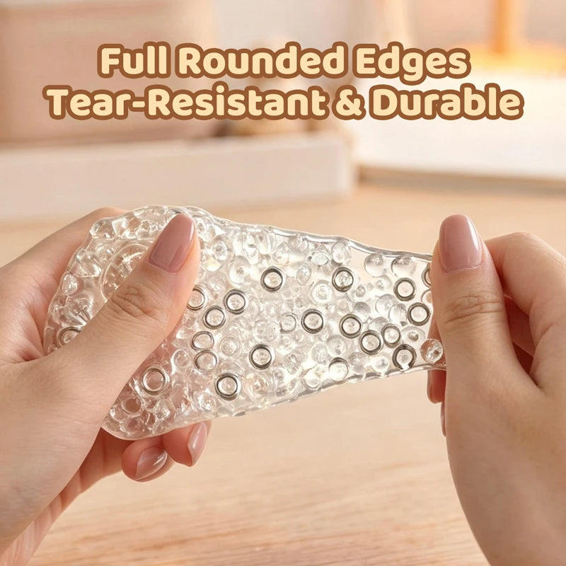 Hands hold a clear, round, tear-resistant silicone stress relief ball on a wooden surface.