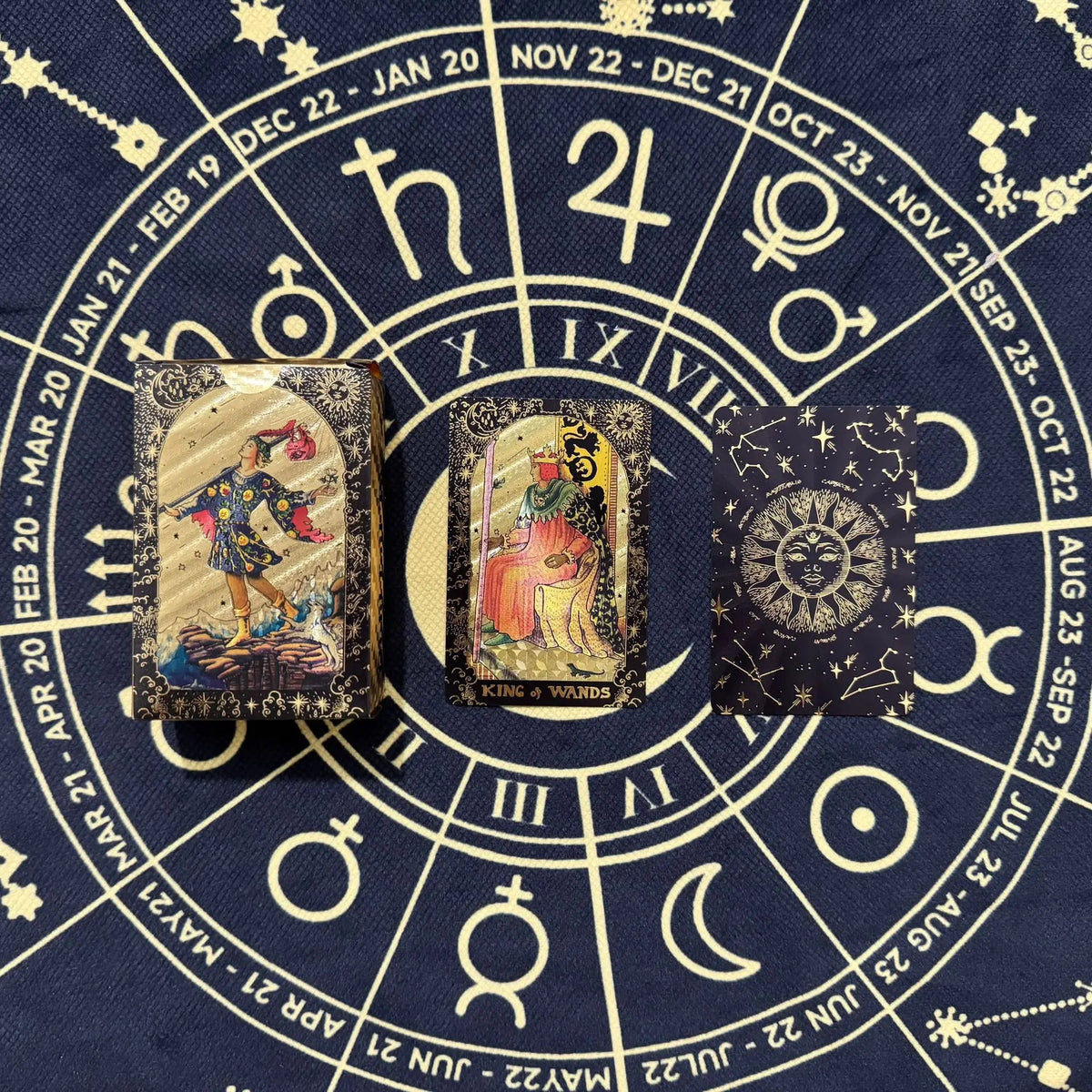 A set of mini gold foil tarot cards laid out on a dark blue fabric with celestial markings.