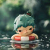 A small mischievous figure from the POP MART Hirono series with light blue hair and a pink face is resting on a reflective su