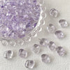 A pile of irregular square geometric glass beads in light purple are scattered on a white surface.
