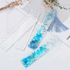 Clear silicone mold for resin bookmarks with blue glitter and silver accents displayed on a white background.