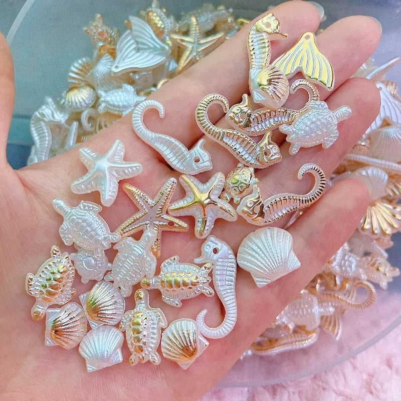 A hand holds a collection of iridescent white and gold ocean animal acrylic beads for DIY jewelry making