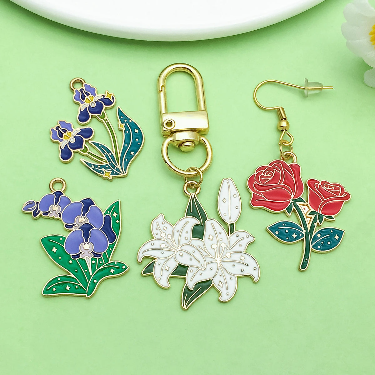 Gold-toned padlock and enamel flower charms featuring blue and red roses and white lilies on a green background.