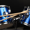 A pair of light wood maple drumsticks resting on a blue and silver drum set.