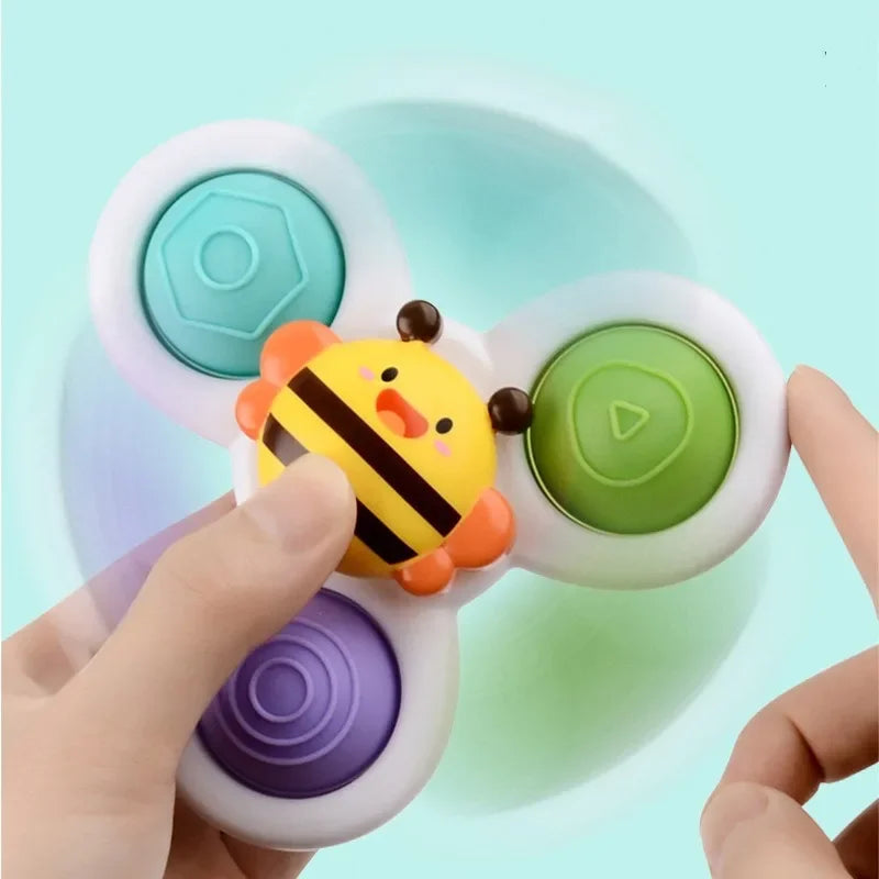 A hand holds a 3-piece baby bath toys set with suction cup spinners featuring yellow and orange designs on a light blue backg