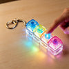 A hand holds a clear plastic keychain featuring multiple colorful LED light-up fidget cubes.
