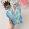 A hand holds a clear plastic storage pouch with a blue zipper and light green fabric, next to other colorful pouches.