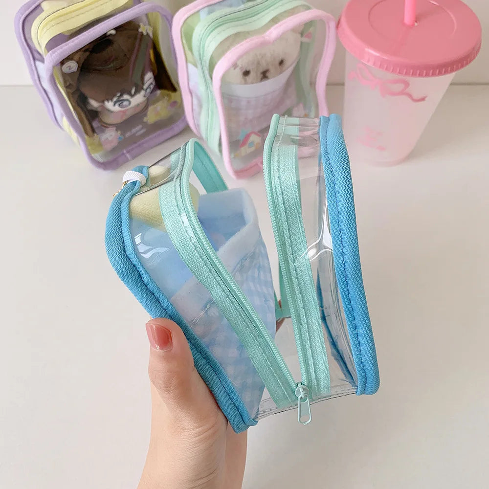 A hand holds a clear plastic storage pouch with a blue zipper and light green fabric, next to other colorful pouches.