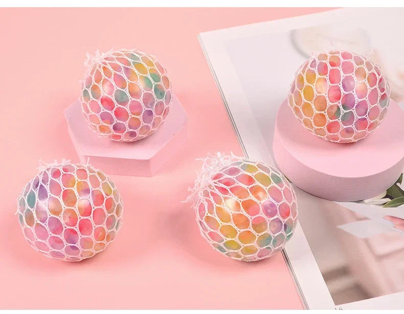 A collection of colorful rainbow squishy stress relief balls resting on a pink surface.