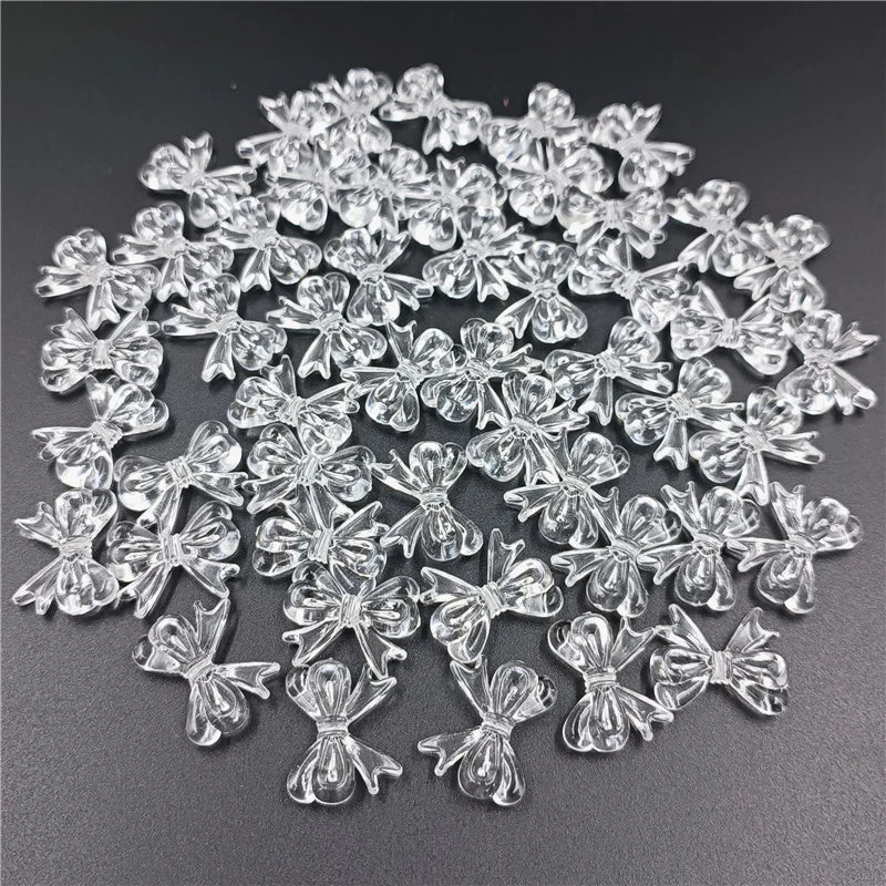 A pile of 20 clear acrylic bow beads for jewelry making scattered on a dark surface.