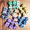 A collection of polyhedral dice in various colors including green, yellow, white, and purple scattered on a wooden surface.