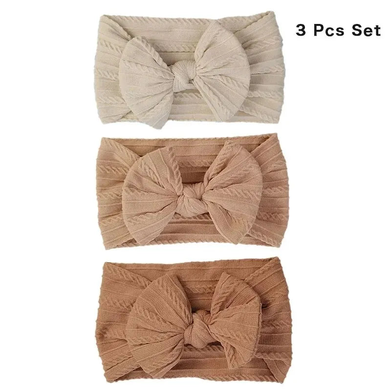 A set of three beige and brown knitted baby headbands with bows