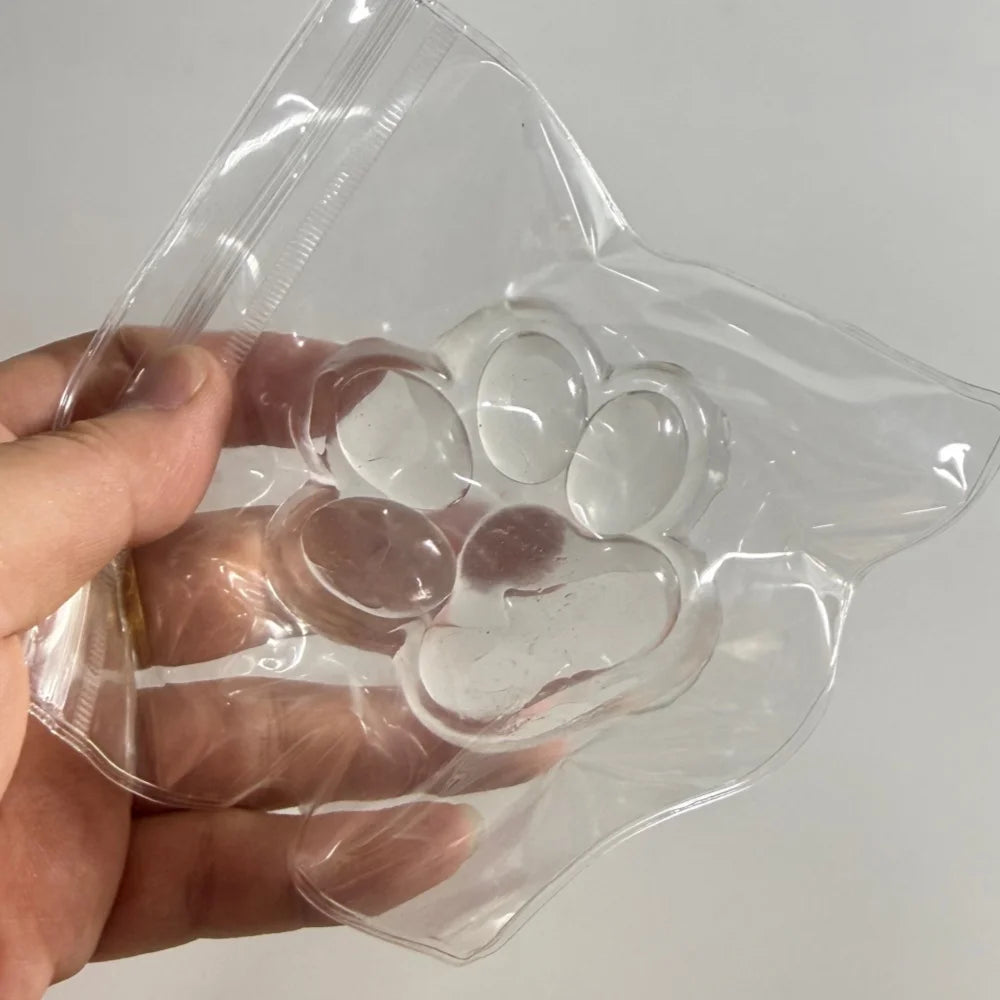 A hand holds a clear plastic silicone cat claw squeeze toy with multiple pads for stress relief and fidgeting.