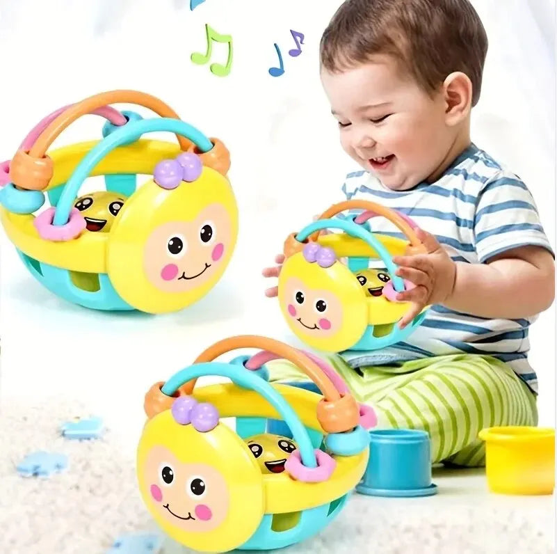 A baby is holding a yellow sensory catch ball rattle toy with purple accents and a blue ring.
