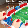 A hand controls a mini tabletop foosball game with four buttons and two hands, featuring red and blue components.