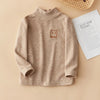 A beige long sleeve shirt for kids featuring a small brown bear embroidery on the chest.