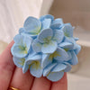 A hand holds a light blue silicone flower blossom mold with yellow accents for crafts and candles.