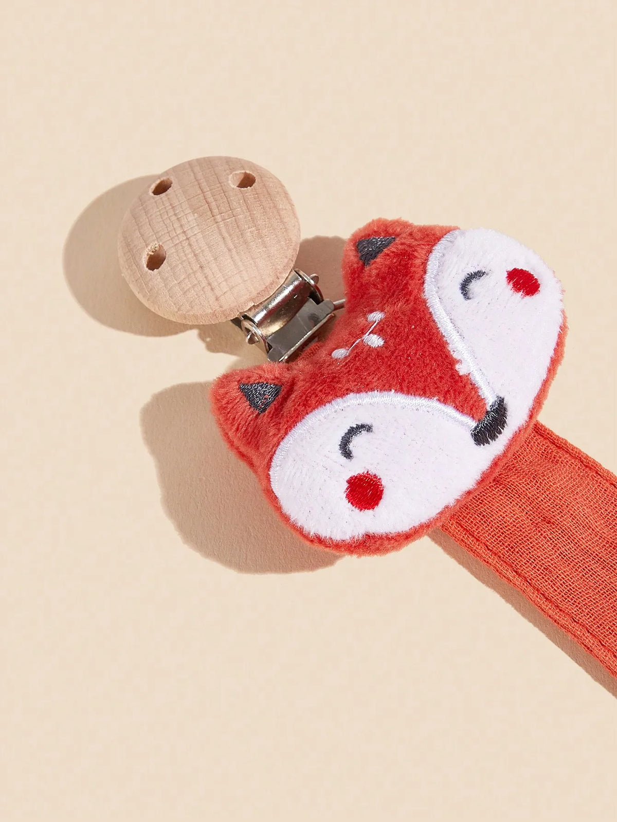 An orange fox-shaped pacifier holder with a wooden top and metal clip against a light background.