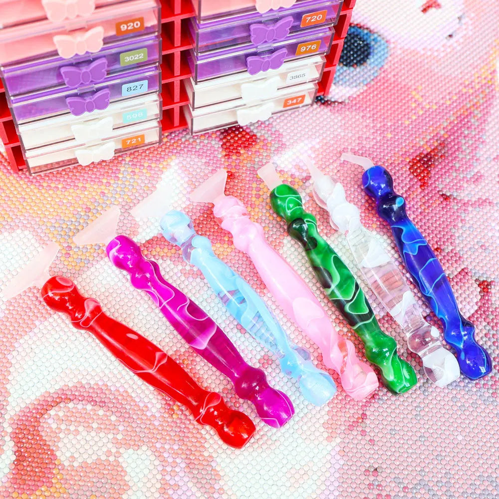 A collection of colorful diamond art pens with interchangeable tips displayed next to a red plastic storage box.