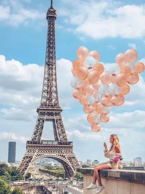A cluster of pink and white balloons is held by a woman in front of the Eiffel Tower.